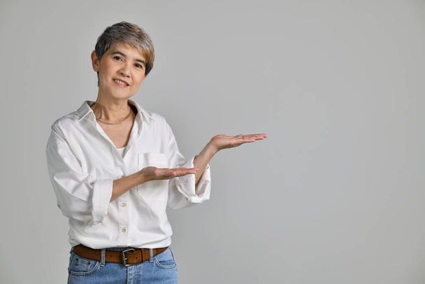 Mujer asiática de mediana edad que muestra espacio de copia vacío en la palma de las manos abiertas para texto o producto aislado sobre fondo blanco. mirando a la cámara - Foto, imagen