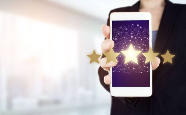 Product service evaluation concept. Hand hold white smartphone with digital hologram five stars sign on light blurred background. Best Excellent Service - Photo, Image