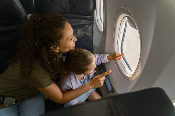 Ευτυχισμένη μητέρα και η κόρη της κοιτάζοντας το τοπίο έξω από το παράθυρο του αεροπλάνου - Φωτογραφία, εικόνα