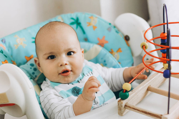Onnellinen hymyilevä poikavauva leikkii leluja syöttötuolissa kotona - Valokuva, kuva