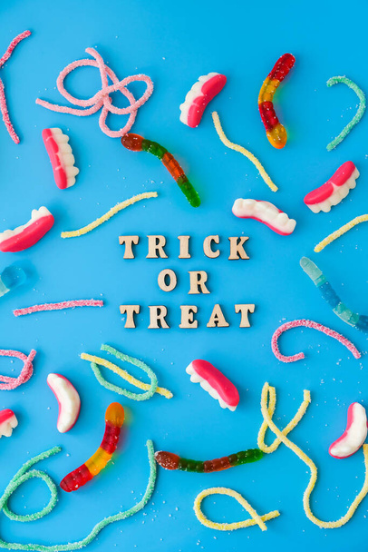 Halloween concept. Halloween party decorations with words TRICK OR TREAT, sweets, top view flat lay on blue background. Greeting card - 写真・画像