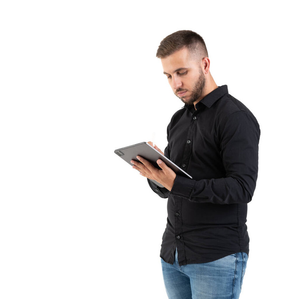 Siyah gömlekli genç adam beyaz arka planda gri bir tablet görüyor. - Fotoğraf, Görsel