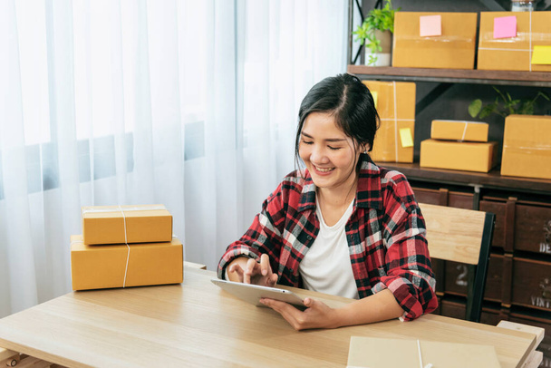 Asian woman startup small business at home office. Online seller entrepreneur young asian woman use tablet checking online order. Woman using tablet check stock goods supply delivery package shipping - Fotografie, Obrázek