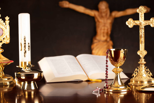 Katholische Symbolkomposition. Religionskonzept. Jesusfigur, Kreuz, Monstranz, Heilige Bibel und goldener Kelch auf grauem Hintergrund.  - Foto, Bild