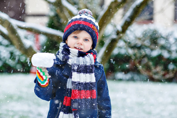 Cute little funny kid boy in colorful winter fashion clothes having fun and playing with snow, outdoors during snowfall - Photo, Image