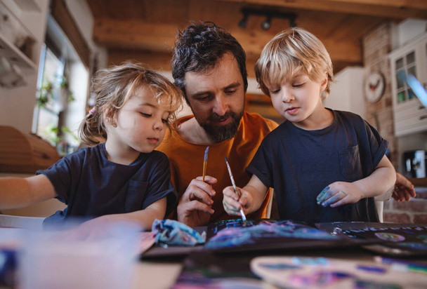 Mature father with two small children resting indoors at home, painting pictures. - Photo, image