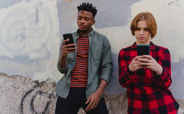 Young biracial couple addicted to smartphones outdoors in town, social media concept - Foto, afbeelding