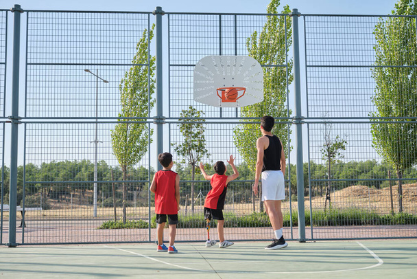 Three brothers playing basketball, one of them has a leg prosthesis. - Foto, Bild