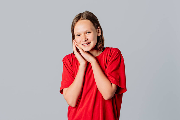 Happy brunette teen girl smiling and laughing pleased, relish something good, daydreaming, wear in casual red t shirt, standing over gray background. Young emotional woman - Valokuva, kuva