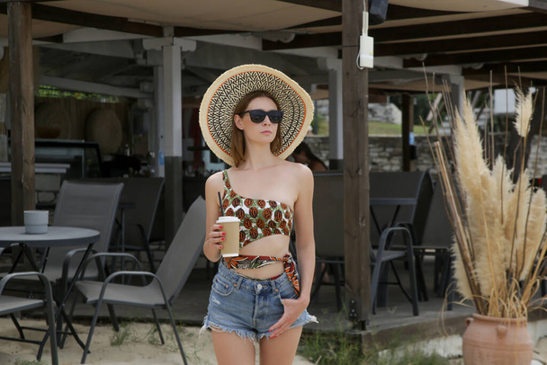Портрет молодої жінки в джинсових шортах і солом'яному капелюсі перед пляжним баром. Розслабляючий літній день у пляжному клубі
. - Фото, зображення