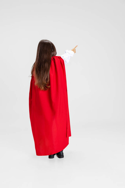 Portrait of little girl wearing red cape standing isolated on white studio background with copyspace for ad. Back view - Foto, Imagen