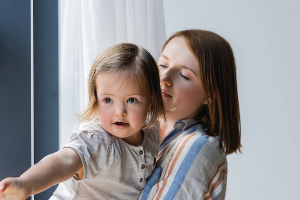 Blurred mother looking at daughter with down syndrome at home  - Foto, imagen