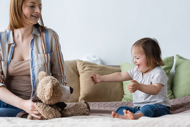Padres sosteniendo juguete suave cerca de la hija excitada con síndrome de Down en la cama  - Foto, Imagen