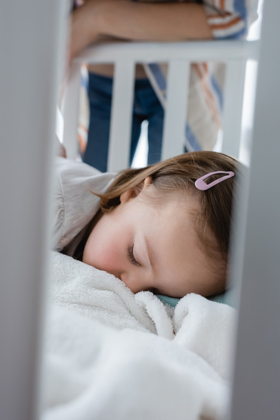Child with down syndrome sleeping in baby crib near mother  - Photo, Image