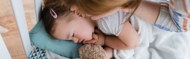 Top view of mom touching sleeping daughter with down syndrome in baby crib, banner  - Photo, Image