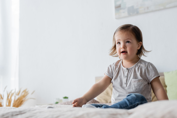 Girl with down syndrome looking away on bed at home  - Fotoğraf, Görsel