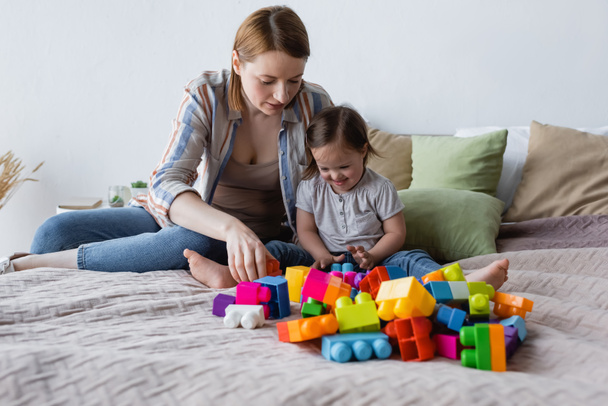 Woman and child with down syndrome playing building blocks on bed at home  - Foto, Imagem