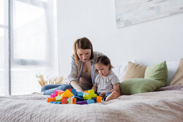 Woman and daughter with down syndrome playing colorful building blocks on bed  - Φωτογραφία, εικόνα