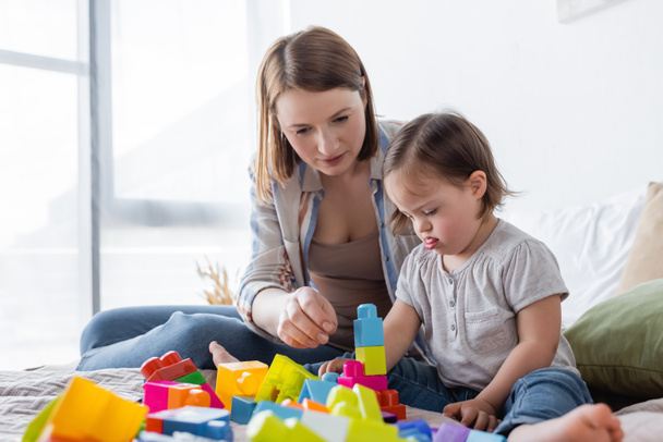 Parent and daughter with down syndrome playing building blocks on bed at home  - Zdjęcie, obraz
