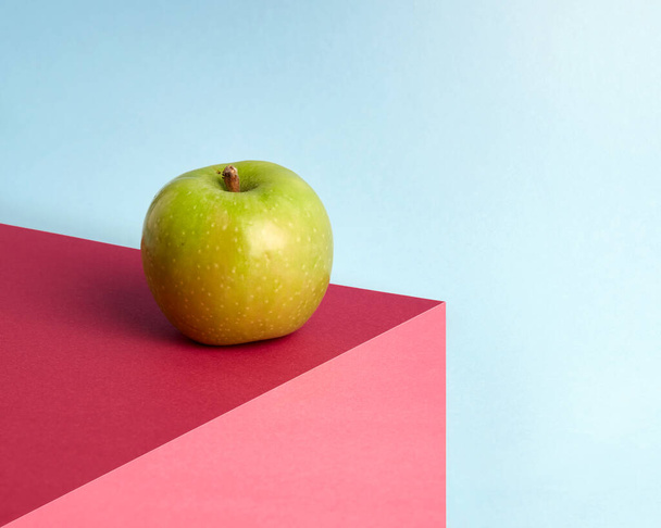 A zöld alma sokszínű, elvont háttérrel rendelkezik. Többszínű lapok illúziója egy volumetrikus állvány. A háttér tartalmaz rózsaszín, sötét rózsaszín és kék színek. - Fotó, kép