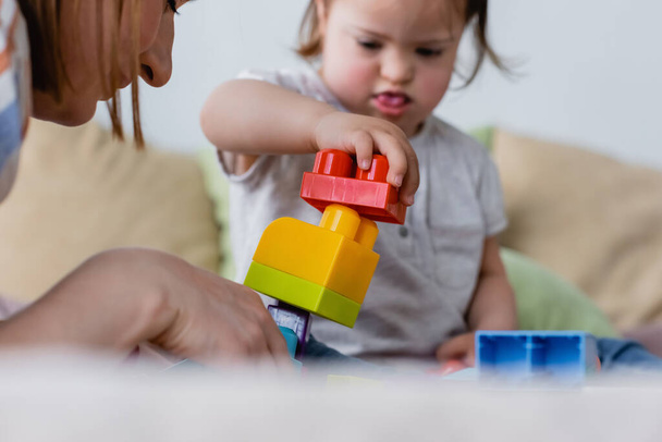 Blurred kid with down syndrome playing building blocks near parent at home  - Foto, imagen