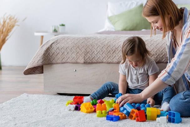 Mother and child with down syndrome playing building blocks on carpet in bedroom  - Valokuva, kuva
