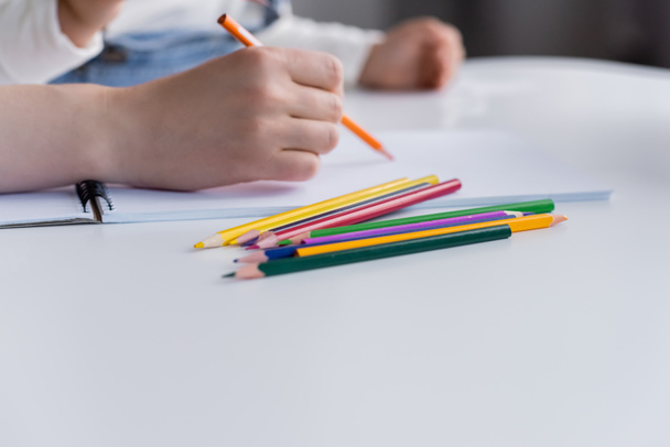 Vista ritagliata di donna disegno vicino bambino sfocato e matite di colore sul tavolo  - Foto, immagini