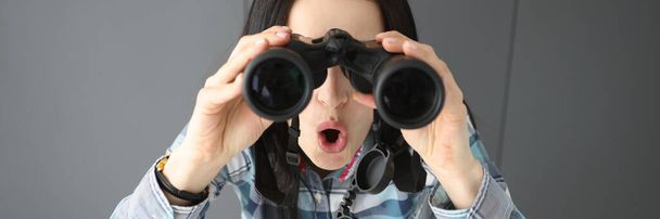 Mulher surpresa abrindo a boca e olhando através de binóculos profissionais pretos - Foto, Imagem