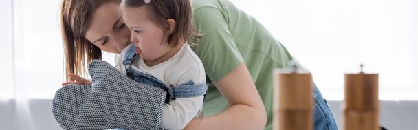 Femme embrasser enfant avec le syndrome du duvet dans le gant de cuisson dans la cuisine, bannière  - Photo, image