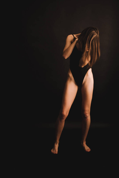 abstrakte Posen auf dem Boden, ein Mädchen im klassischen Body, das intuitiv auf schwarzem Hintergrund tanzt, verschwommene Fotos und Unschärfen, Bildrauschen, unfokussierte Ganzkörperporträts - Foto, Bild