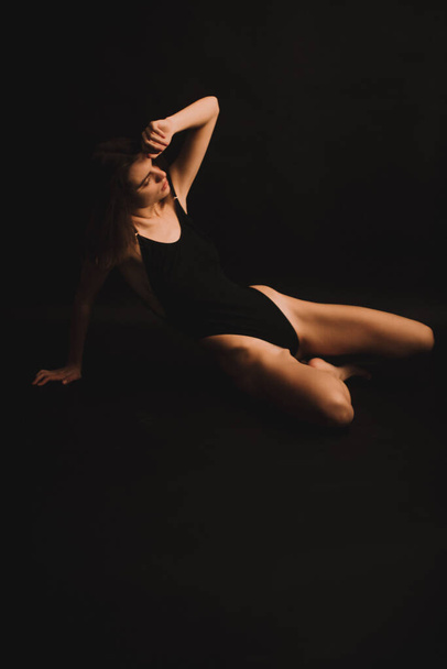 a brunette girl in a candid bodysuit freely expresses emotions and dances on camera. photo shoot on a black background - Foto, afbeelding