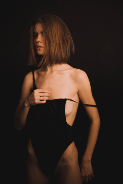 a brunette girl in a candid bodysuit freely expresses emotions and dances on camera. photo shoot on a black background - Φωτογραφία, εικόνα