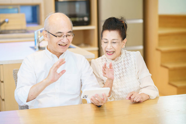Seniorenpaar kommuniziert online mit Smartphone im Zimmer - Foto, Bild