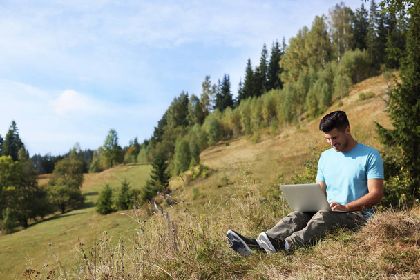 Man working with laptop outdoors surrounded by beautiful nature. Space for text - Photo, Image