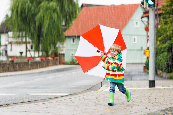 schönes Kind mit rotem Regenschirm und bunter Jacke im Freien - Foto, Bild