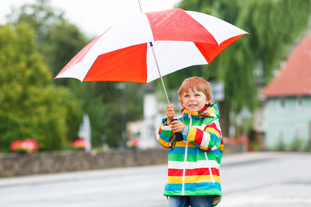 όμορφο παιδί με κίτρινο ομπρέλα και υπαίθρια πολύχρωμο σακάκι - Φωτογραφία, εικόνα