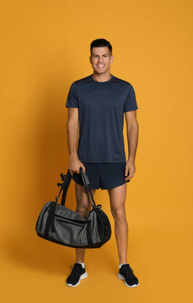 Handsome man with sports bag on yellow background - Fotoğraf, Görsel