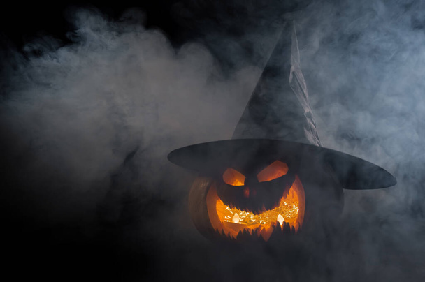 A creepy pumpkin with a carved grimace in the smoke. Jack o lantern in the dark. - Fotografie, Obrázek