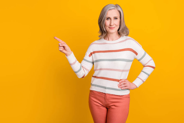 Photo of pretty adorable lady pensioner wear striped pullover pointing finger empty space smiling isolated yellow color background - Fotografie, Obrázek