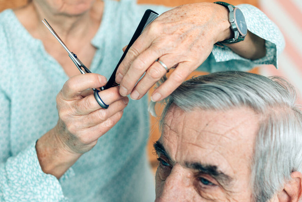 hands of elderly woman haircuts a senior man - home assistance or voluntary assistance - taking care of other - couple life in the third age - Valokuva, kuva
