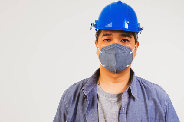 El guapo trabajador masculino llevaba un casco azul y una máscara antipolvo para prevenir la PM2.5 y la epidemia de COvid-19. - Foto, Imagen