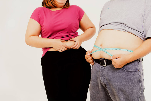 Pary z otyłych i otyłych rozmiarów ścisnąć nadmierną talię i użyć taśmy talii do porównania ich nadmiar tłuszczu: Pojęcie otyłość mężczyzn i kobiet, którzy nie są zdrowe. - Zdjęcie, obraz