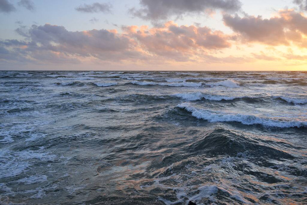 Baltic sea shore under a blue sky with glowing pink and golden sunset clouds after the storm. Crashing waves. Nature, environmental conservation, ecotourism. Picturesque panoramic scenery - Photo, Image