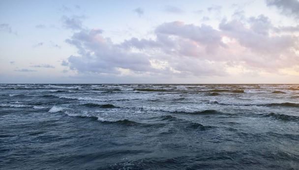 Fırtınadan sonra parlayan günbatımı bulutlarıyla mavi gökyüzünün altında Baltık Denizi kıyısında. Su yüzeyi dokusu, çarpan dalgalar. Doğa, çevre koruma, eko-turizm. Resimli panoramik manzara - Fotoğraf, Görsel