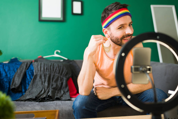 Hispanic queer henkilö laittaa korvakorut ja koruja tehdessään hänen meikki video kauneus opetusohjelma - Valokuva, kuva