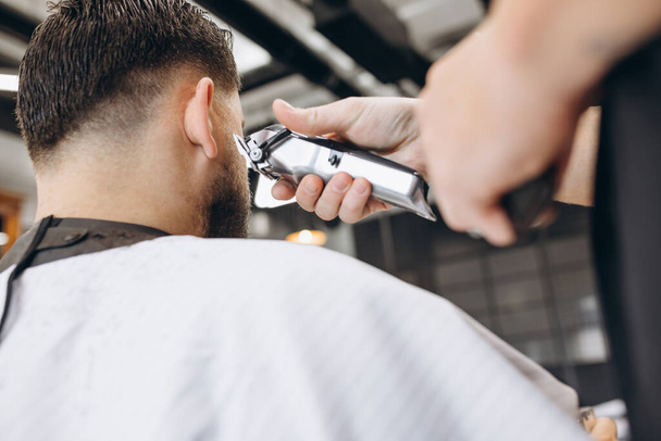 Close-up professional barber cuts the hair, beard of man at barbershop. Beauty, selfcare, style, fashion, healthcare and male cosmetics concept. - Photo, image
