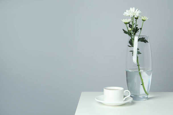 Jarrón con crisantemos y taza de café sobre mesa blanca. - Foto, Imagen