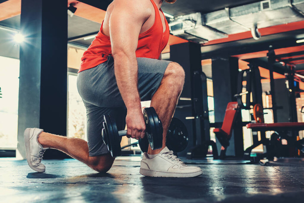 Közelről sportoló férfi edzés súlyzókkal a tornateremben. Guggolás. Alacsony látószögű. A fitnesz és az edzés fogalma. - Fotó, kép