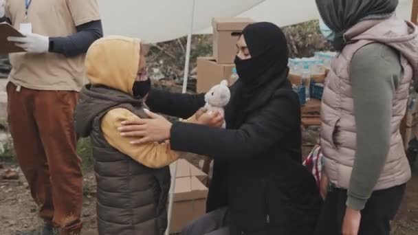 Medium shot van moslim vrouw in zwarte nicht verzorgen van dochter, het aantrekken van warme kleren aan haar, wonen in tenten in arme vluchtelingenkamp - Video