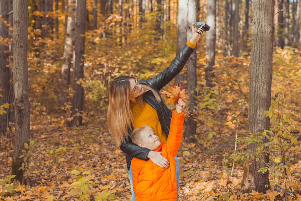 Son and mother are taking selfie on camera in autumn park. Single parent, leisure and fall season concept. - Photo, Image